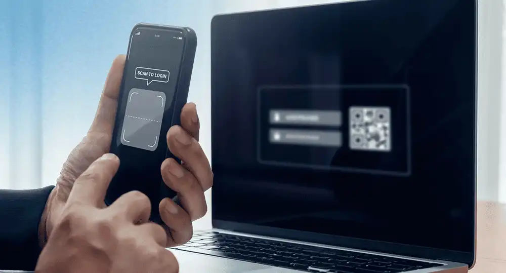 Usuario escaneando código QR con smartphone para inicio de sesión seguro sin contraseña en laptop.